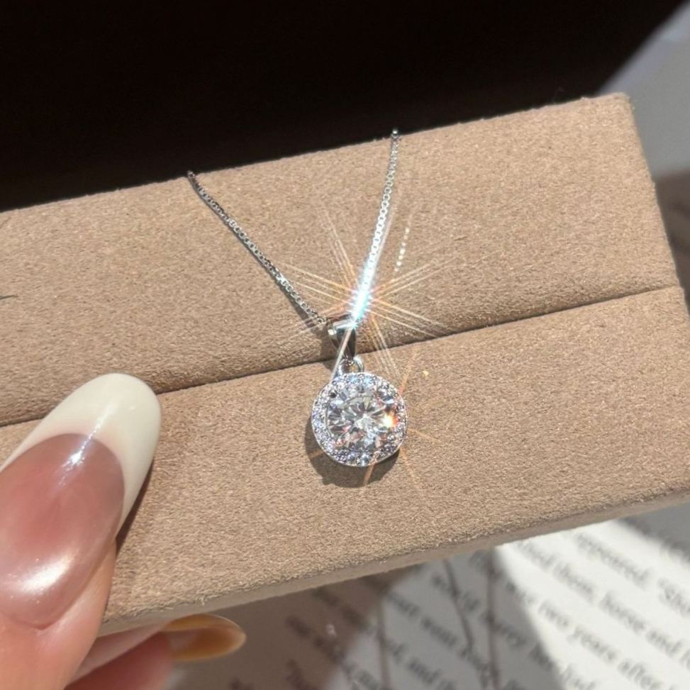 Moissanite halo pendant necklace held in hand over a jewelry box